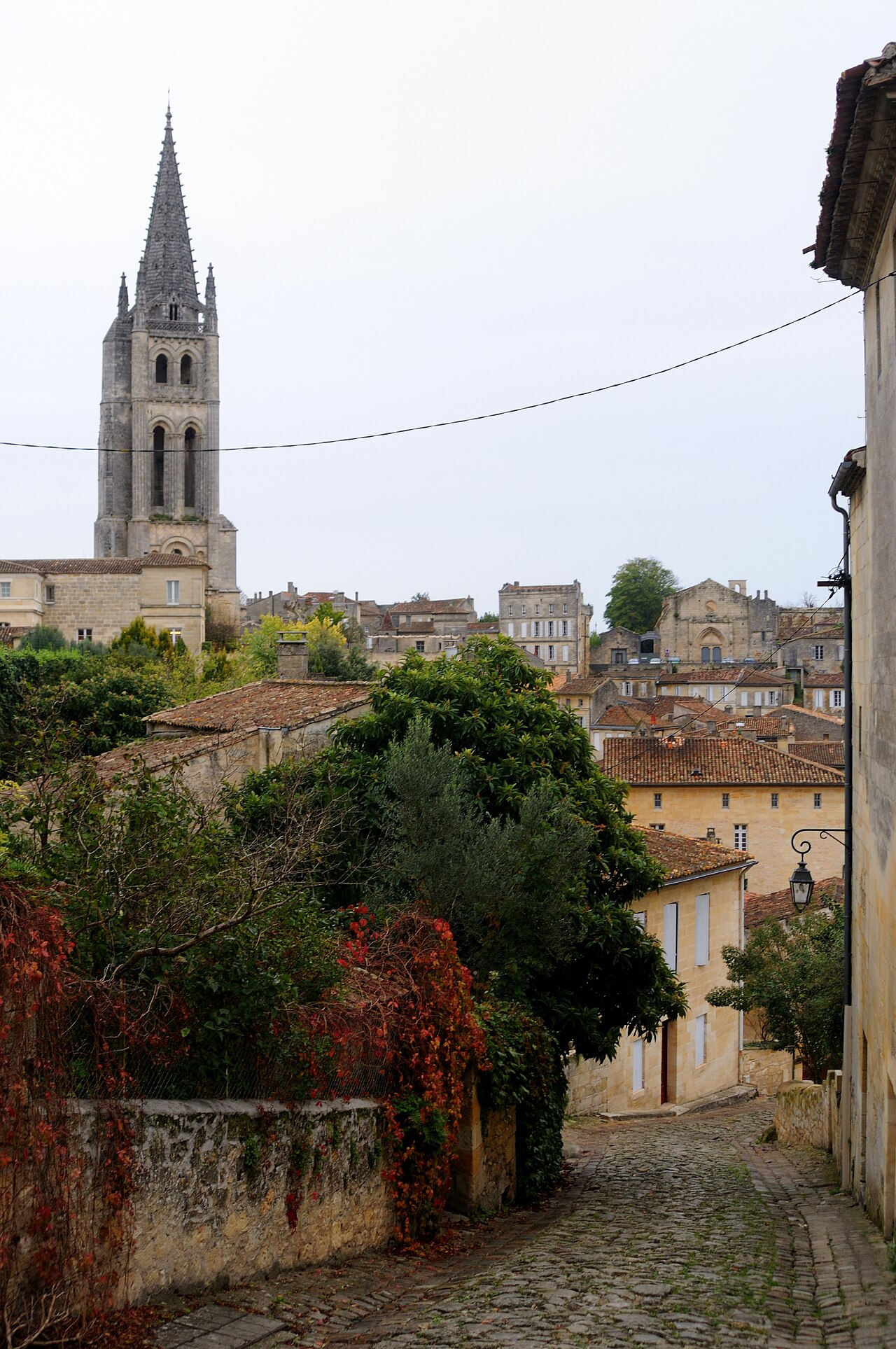 A cobbled lane winding between stone houses toward Saint-Émilion’s monolithic church bell tower